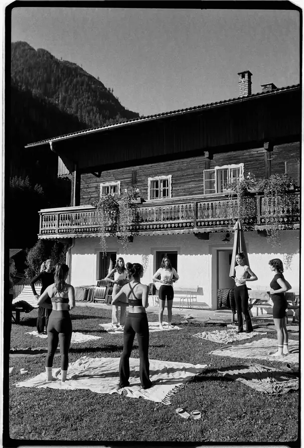 Black and white film photo of a pilates class in front of a wooden chalet
