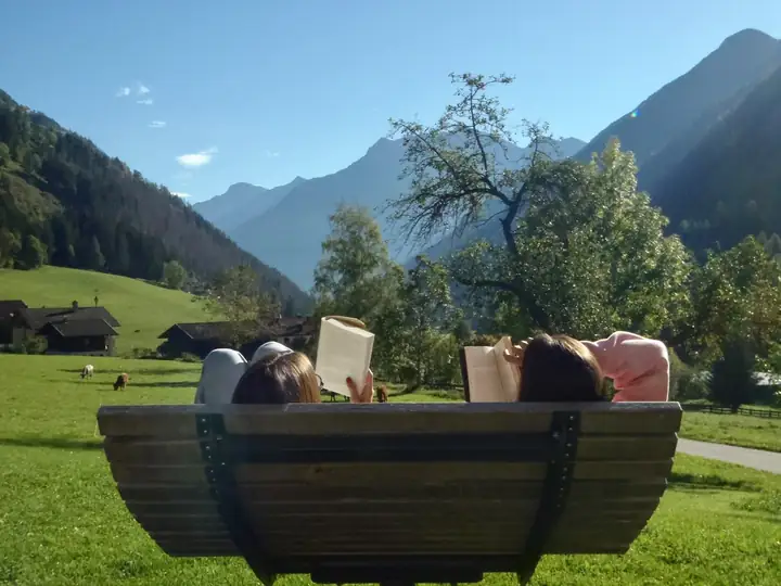 Two women reading on a wooden bench facing the mountains